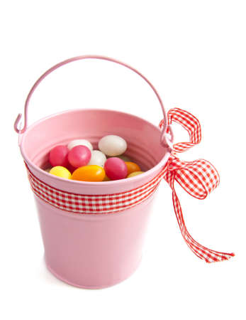 Pink bucket with colorful candy eggs over whiteの写真素材