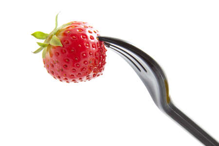 Delicious fresh strawberry on a black fork over whiteの写真素材