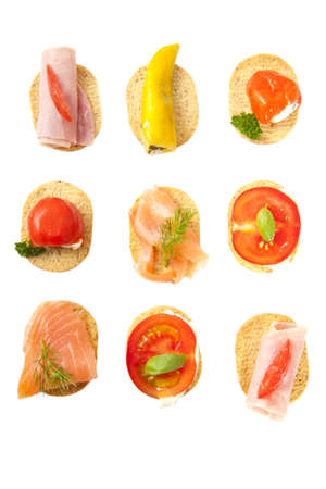 Little snacks with cheese vegetables meat and fish in a row over whiteの写真素材
