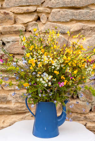 Bouquet field flowers in blue watering can in front of a stone backgroundの写真素材