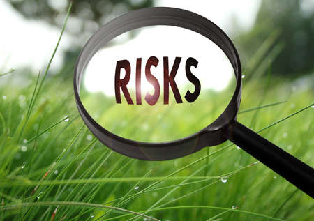 Magnifying glass with the word risks on grass background. Selective focusの写真素材
