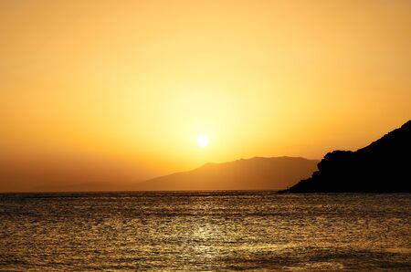 Landscape of a golden sunset in a beach in the Mediterranean. Sun disappearing behind the mountains.の写真素材