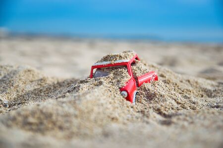 Red Mini toy vehicle buried in the sand of the beach.の写真素材