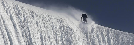 Solo mountaineer navigating a challenging snowy ridge against a foggy sky. Climber trekking icy mountain ridge through dense fogの写真素材