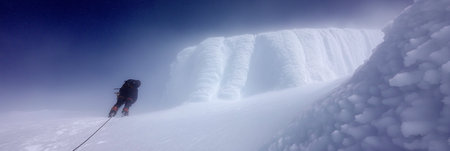 Solo mountaineer navigating a challenging snowy ridge against a foggy sky. Climber trekking icy mountain ridge through dense fogの写真素材