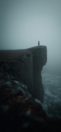 Figure on a cliff overlooking waves in a gloomy, mysterious, and atmospheric landscape. Lone figure standing on a cliff edge facing a dark, misty seaの写真素材