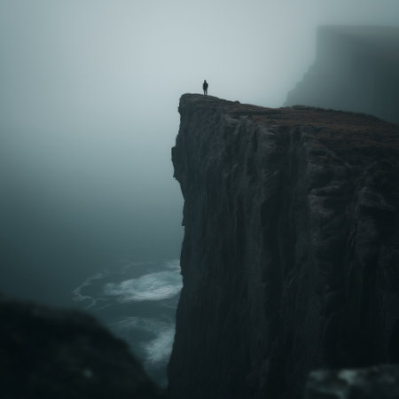 Figure on a cliff overlooking waves in a gloomy, mysterious, and atmospheric landscape. Lone figure standing on a cliff edge facing a dark, misty seaの写真素材
