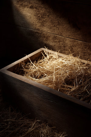 Empty wooden manger with straw receiving warm light, symbolizing birth and new beginnings. Wooden manger with straw under soft spot lightの写真素材