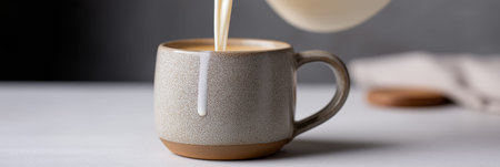 Creamy dairy milk pouring from a pitcher into a ceramic mug on a gray table. Milk pouring from pitcher into ceramic mugの写真素材