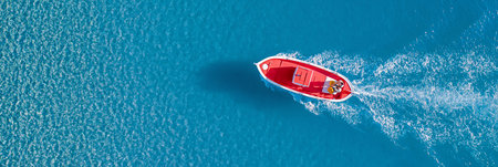 Small red boat navigating open ocean, leaving white wake on clear blue water. Red speed boat cruising clear blue water