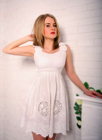 beautiful blond girl with blue eyes in a white dress looks strictly on a white backgroundの写真素材