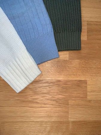 part of the sleeves of knitted sweaters on a wooden surface. white, blue aand green knitted...