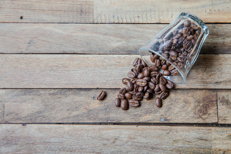 Coffee beans in a glass toppled over and spilled on wooded tableの写真素材