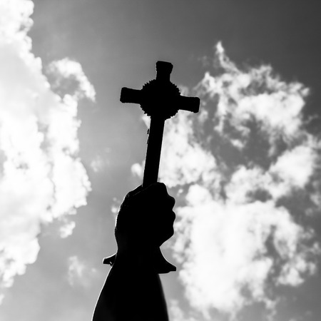 Silhouette of Hand holding cross in the sky, focus at the crossの写真素材