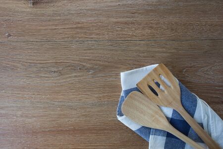 Wooden kitchen utensils and linen kitchen towels on light wood tabletop, with copy space in the...