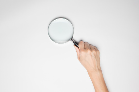 A female(woman) hand hold a magnifier(reading glass) isolated white at the studio.の写真素材