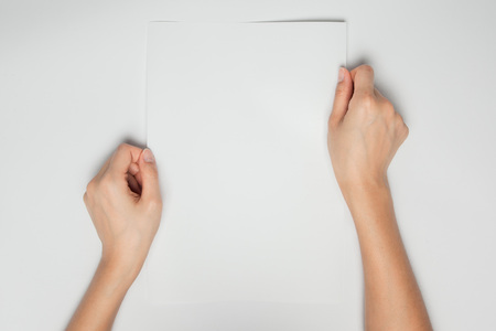 A female(woman) hands hold a empty(blank) white paper isolated white, top view at the studio.の写真素材