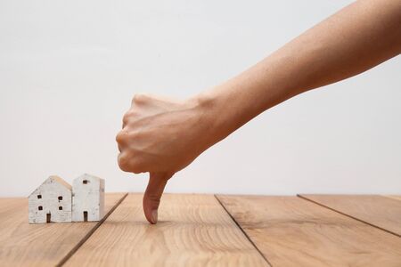 Real estate concept a hand showing thumb down at miniature houseの写真素材