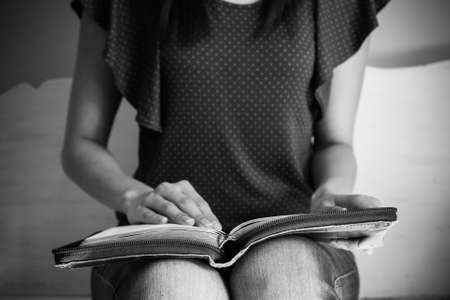 Closeup of a young woman reading a large bible, focus on the bible.の写真素材