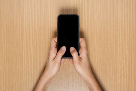 woman hand holding smart phone on wood backgroundの写真素材