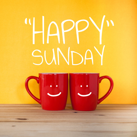 Happy sunday word.Two cups of coffee and stand together to be heart shape on yellow background with smile face on cup.の販売画像