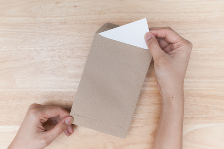 Hands holding brown envelope with a empty paper on wood backgroundの写真素材