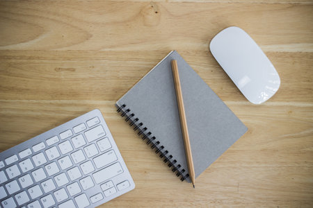 A white keyboard, notebook and a mouse on a wooden table.の写真素材