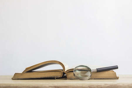 An old book with a magnifying glass on a wooden table.の写真素材
