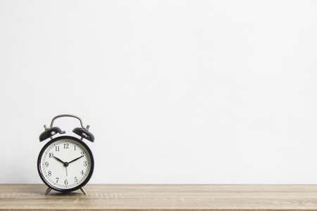 Clock on wooden table over the light wall.の写真素材