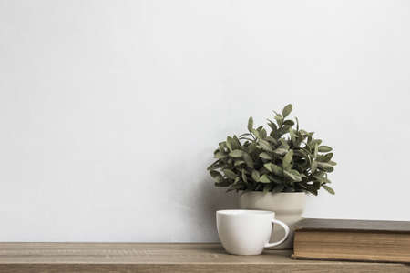 A plant with coffee cups and bible on a wooden table.