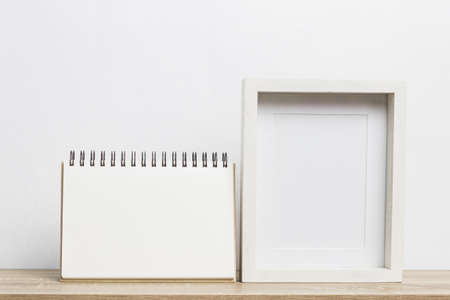 Mock up white note and photo frame on a wooden table over the white wall.