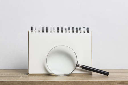 Mock up white note and magnifying glass on a wooden table over the white wall.の写真素材