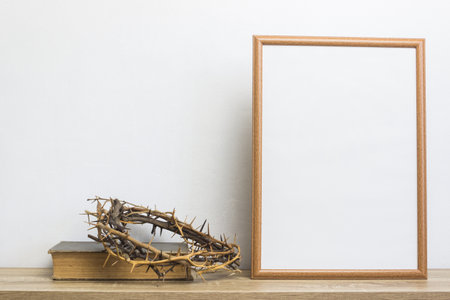 A bible with thorn crown and a white photo frame on a table.