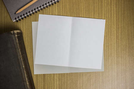 Books with notebook and white paper on a wooden table.