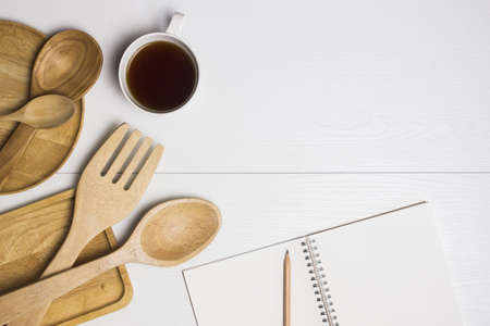 Wooden utensil with notebook and coffee over a white table.