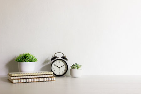 Office desk table with book, alarm clock and plant on white wall background.の写真素材