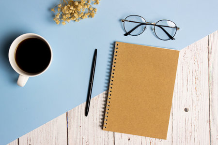 Writing concept with brown notebook, coffee cup, glasses and flowers over blue and wooden background.の写真素材
