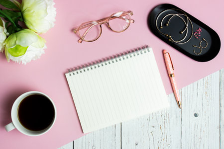 Women working items with notebook, coffee cup, glasses and roses over pink and wooden table.の写真素材