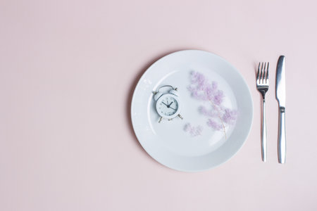 Eating healthy concept with clock, knife and fork over the pink background.の写真素材