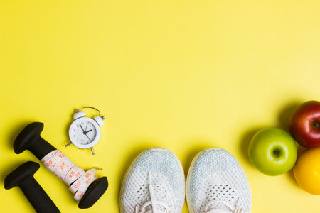 Work out concept with oranges, clock, sneakers and dumbbell over the yellow background.の写真素材