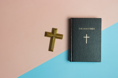 Holy Bible with a wooden cross on pink and blue background with copy space.