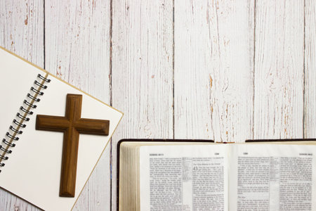 A dark wooden cross with notebook over the wooden table with copy space.の写真素材