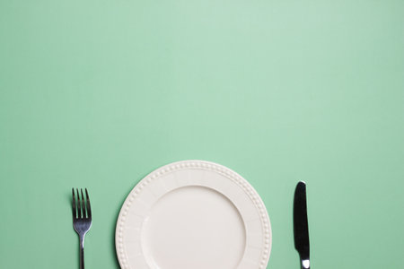 A white plate with fork and knife on green background with copy space.の写真素材