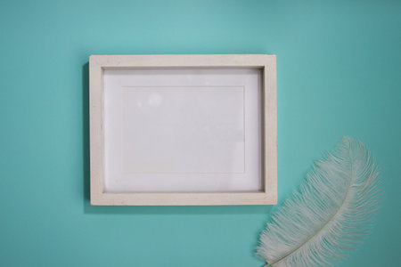 A white wooden frame with white feather on green background.の写真素材