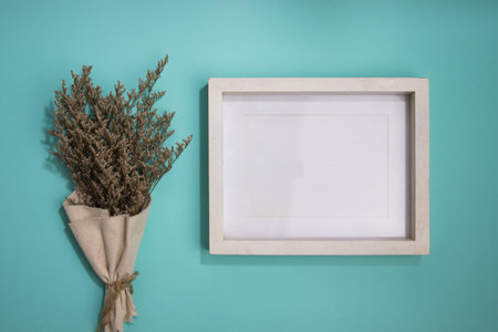 A blank white wooden frame with flower bouquet over the mint background.の写真素材