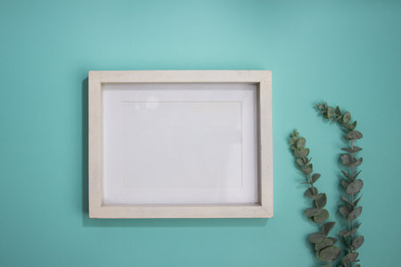 A white frame with green leaves on a mint background.の写真素材