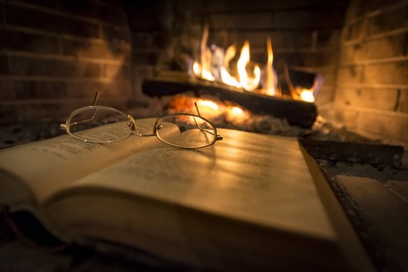 open book with glasses on it beside fireplaceの写真素材