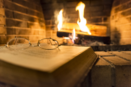 open book with glasses on it beside fireplaceの写真素材