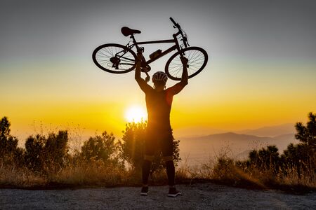 Male biker holds bike above head after successfully biking up a hill at sunsetの写真素材
