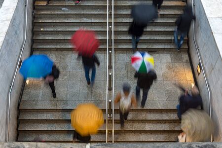 overhead view of people walking towards and away from the entrance to the underground train station under rain with umbrellas - bad weatherの写真素材